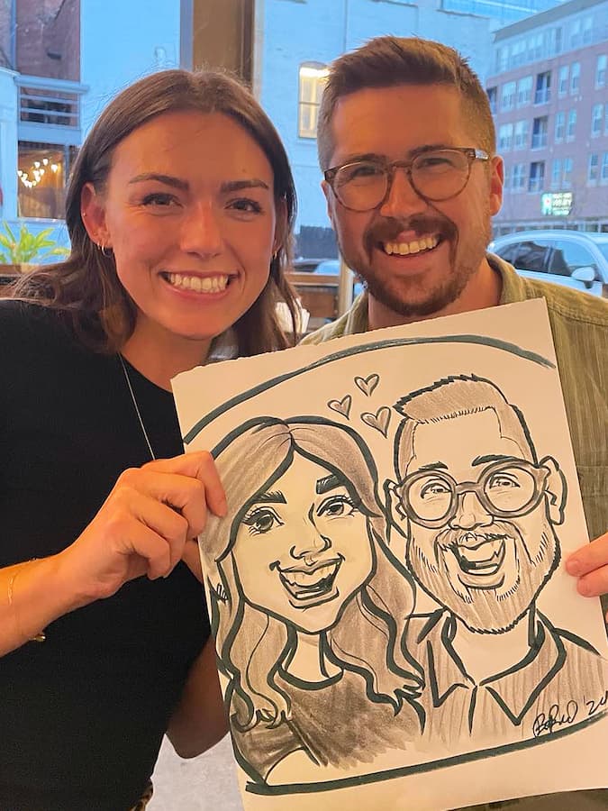 An engaged couple who were looking for a caricature artist for their wedding are seen holding up their demo caricature and smiling.